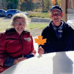 Two volunteers at KLT's 2025 Thanks.Giving event holing a fallen Sugar Maple leaf.
